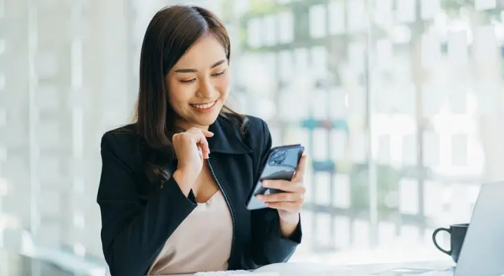 A woman is smiling while looking at her phone.