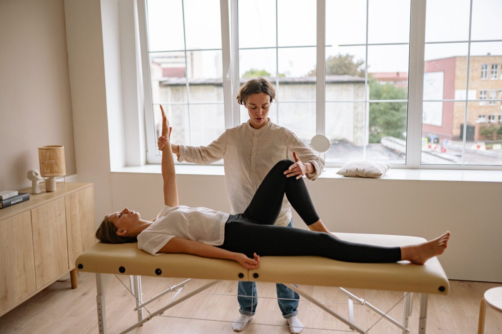 A woman is stretching on the bed while another person watches.