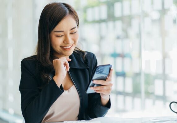 A woman is smiling while looking at her phone.